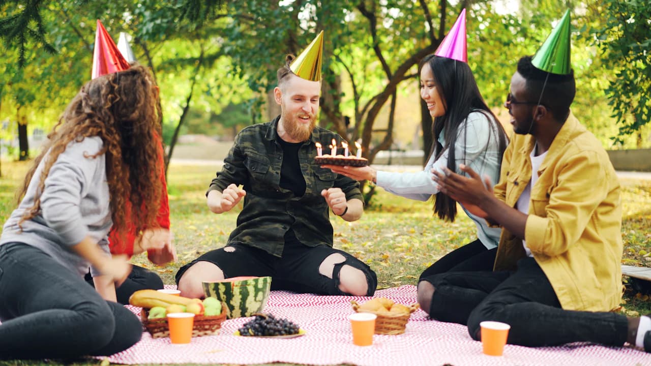 Friends sharing a birthday cake at an outdoor picnic